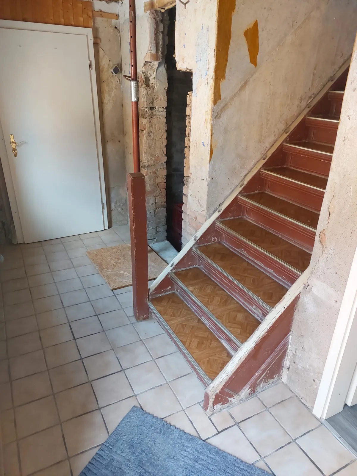 Altes Treppenhaus mit roter Holztreppe und gefliestem Boden vor der Sanierung in Irxleben